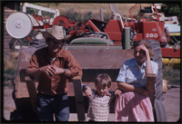 Family Photo: Don, Lane and Ruth Huddlestone outside, with farm equipment surrounding.